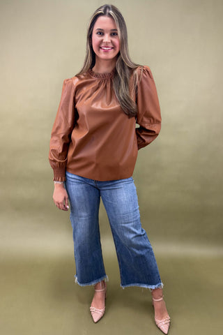 Woman wearing a brown blouse and blue jeans against a green background