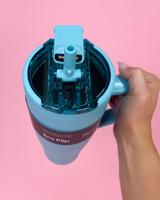Blue and pink water bottle with a hand holding it against a pink background