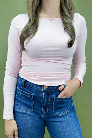 Person wearing a light pink long-sleeve top and blue jeans against a green background