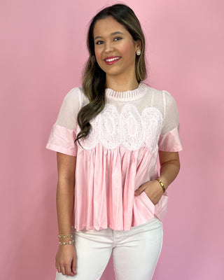 Woman wearing a pink peplum top and white pants against a pink background