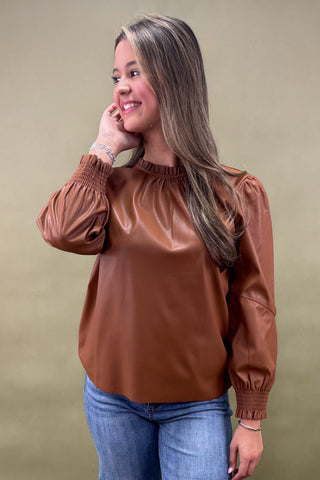 Woman wearing a brown blouse and blue jeans against a beige background