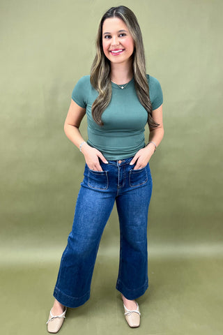 Woman wearing a green top and blue jeans against a green background