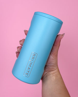Hand holding a blue tumbler with 'BRUMATE' branding against a pink background