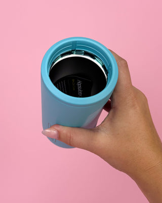 Hand holding a blue tumbler against a pink background