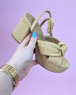 Hand holding a woven sandal against a purple background