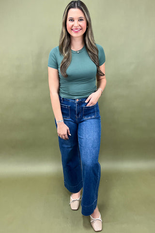 Woman wearing a green t-shirt and blue jeans against a plain background