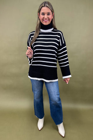 Woman wearing a black and white striped sweater with blue jeans on a green background
