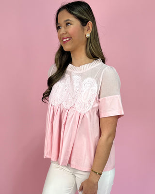 Woman wearing a pink and white blouse with lace details against a pink background