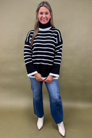 Woman wearing a black and white striped sweater with blue jeans on a beige background
