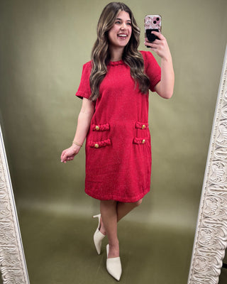 Woman taking a mirror selfie wearing a red dress with gold buttons on a green background