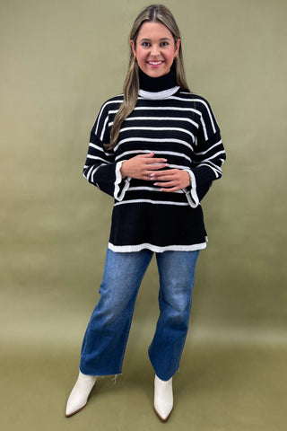 Woman wearing a black and white striped sweater with blue jeans on a green background