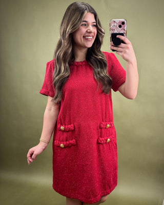 Woman taking a mirror selfie wearing a red dress with gold buttons on a green background