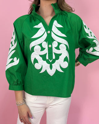 Green blouse with white patterns worn by a person on a pink background