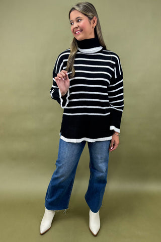 Woman wearing a black and white striped sweater with blue jeans on a green background