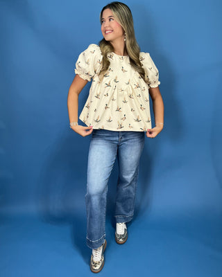 A woman modeling a cream-colored short-sleeve peplum top with a small bird print