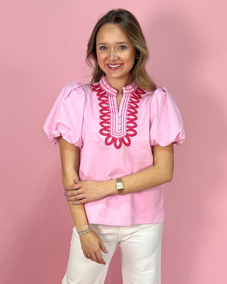 Woman wearing a pink blouse with red embroidery against a pink background