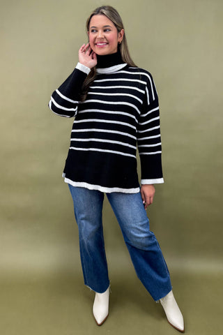 Woman wearing a black and white striped sweater with blue jeans against a green background