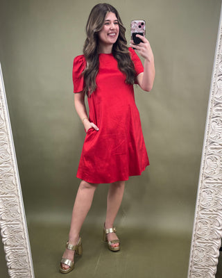 Woman taking a mirror selfie wearing a red dress on a green background