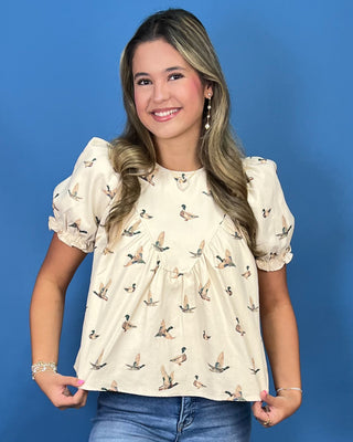 A smiling young woman wearing a cream-colored short-sleeve blouse with a brown and black duck print