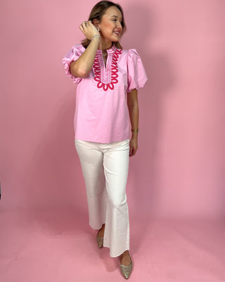 Woman wearing a pink blouse with white pants against a pink background