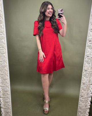 Woman in a red dress taking a mirror selfie against a green wall.
