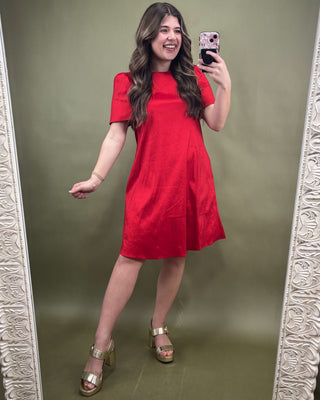 Woman in a red dress taking a mirror selfie against a green wall.