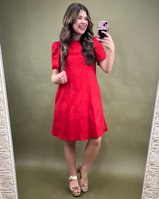 Woman taking a mirror selfie wearing a red dress on a green background