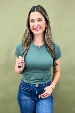 Woman wearing a green ribbed top and blue jeans against a green background