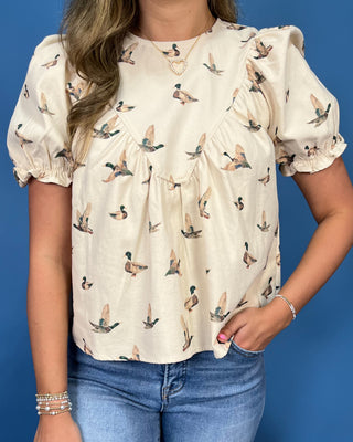 A woman wearing a cream-colored short-sleeve blouse with a brown and green duck print