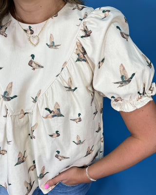 A close-up of a person wearing a cream-colored puff-sleeve top with an all-over duck print