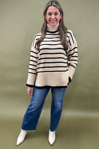 Woman wearing a striped sweater and blue jeans against a green background
