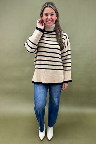 Woman wearing a striped sweater and blue jeans against a green background