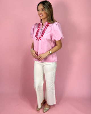 Woman wearing a pink blouse with white pants against a pink background