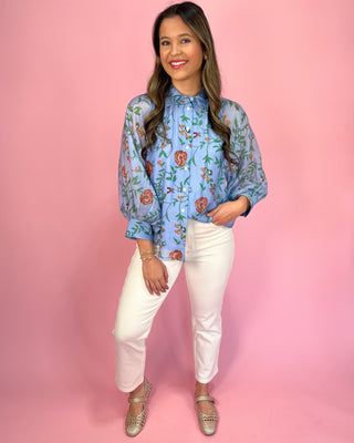 Woman wearing a floral blouse and white pants against a pink background