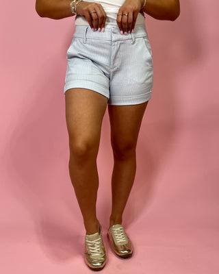 Person wearing light blue shorts on a pink background