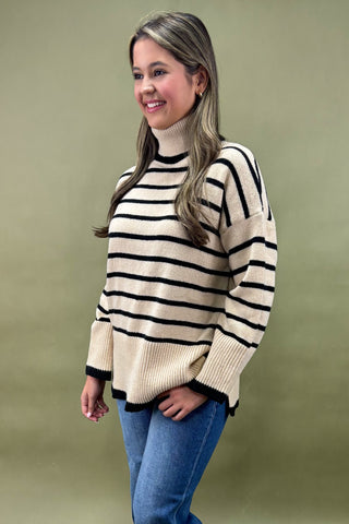 Woman wearing a striped sweater and blue jeans against a green background