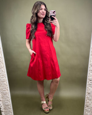 Woman taking a mirror selfie wearing a red dress on a plain background