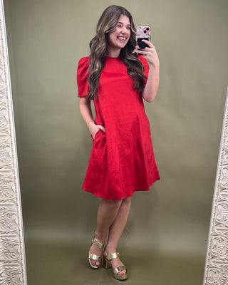Woman taking a mirror selfie wearing a red dress on a green background