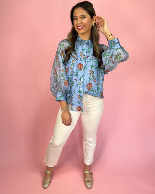 Woman wearing a floral blouse and white pants against a pink background