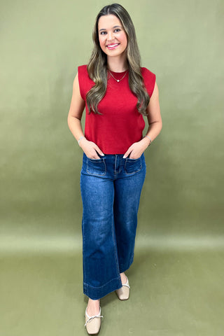Woman wearing a red sleeveless top and blue jeans against a green background