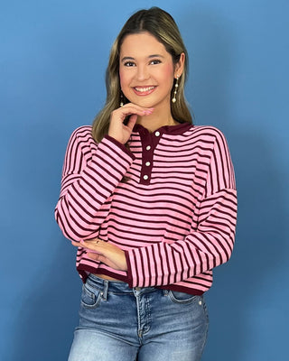 A woman modeling a pink and burgundy striped long-sleeve henley top with blue jean