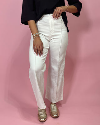 Person wearing white pants and a black top on a pink background