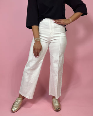 Person wearing white pants and black top on a pink background
