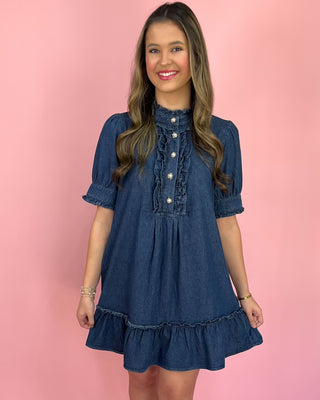 Woman wearing a blue denim dress against a pink background