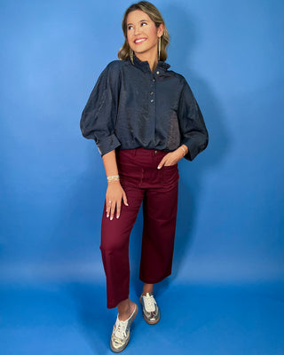 Navy satin blouse with a ruffled mock neckline, partial button front, and relaxed three-quarter sleeves.