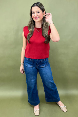 Woman wearing a red sleeveless top and blue jeans against a green background