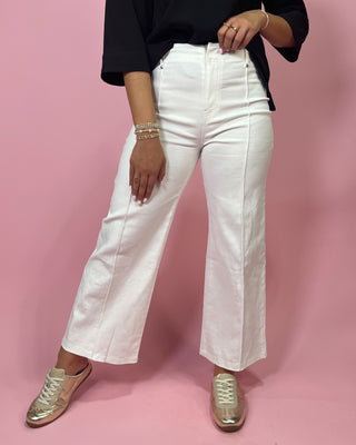 Person wearing white jeans and gold shoes on a pink background