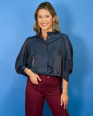 Navy satin blouse with a ruffled mock neckline, partial button front, and relaxed three-quarter sleeves.