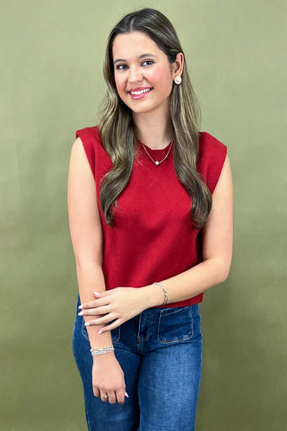 Woman wearing a red sleeveless top and blue jeans against a green background