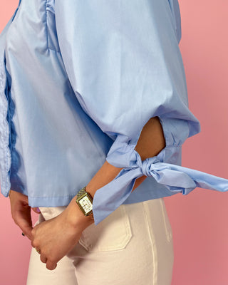 Person wearing a light blue blouse with tied sleeves against a pink background